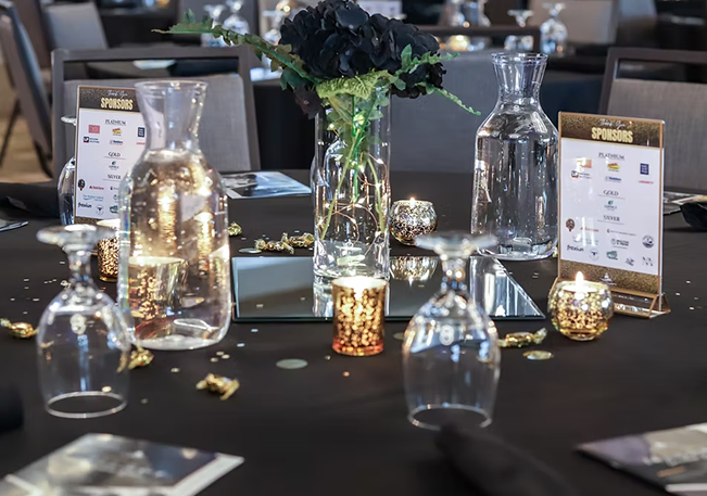 Black-linen banquet table set with candles and glassware for a corporate awards dinner
